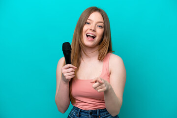 Singer caucasian woman picking up a microphone isolated on blue background surprised and pointing front