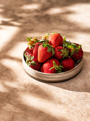 Strawberries in plate on brown textured background with window shadows, text space