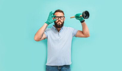 Young handsome man wearing plumber uniform holding toilet plunger looks happy. Professional...