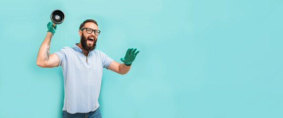 Young handsome man wearing plumber uniform holding toilet plunger looks happy. Professional...