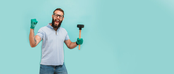 Young handsome man wearing plumber uniform holding toilet plunger looks happy. Professional...