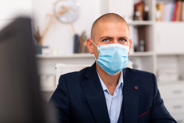 Portrait of young man manager in medical mask standing in modern office