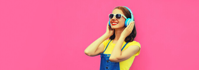 Portrait of happy smiling young woman with headphones listening to music on pink background, blank copy space for advertising text