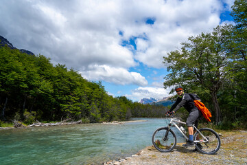 Fototapeta premium man on the bike in the forest next to the river with mountains in the background