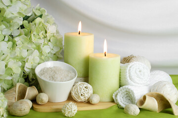 Fototapeta na wymiar spa concept of soft green orchid flower with burning candles surrounded in natural dried elements, white towels, bath salts against a white elegant swooped background. Spa still life