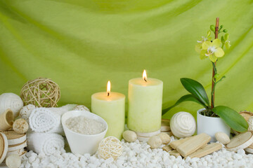 Fototapeta na wymiar spa concept of soft green orchid flower with burning candles surrounded in natural dried elements, white towels, bath salts against an elegant green swooped backdrop.