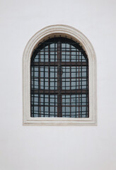 Antique old window with black iron bars framed on a light gray wall. The Jesuit Church in Lviv.