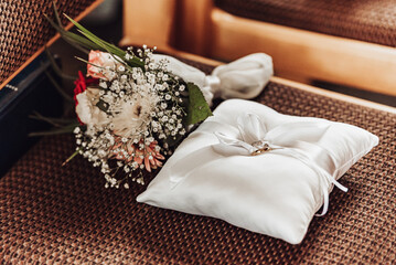 Silver wedding rings on a white pillow and a bridal bouquet