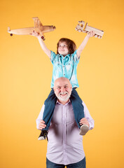 Young grandson and old grandfather piggyback playing with plane and wooden toy truck. Men generation granddad and grandchild.