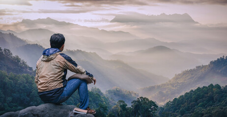 Young male sitting on top of cliff in summer mountains enjoying Sunset or Sunrise Colorful Sky.