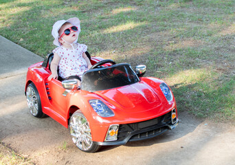 Obraz na płótnie Canvas Caucasian baby in a white hat riding in an electric convertible red sports car. child driving a car on a summer day