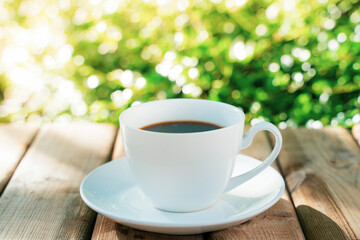 white ceramic coffee mug On the wooden floor, green tree bokeh background.