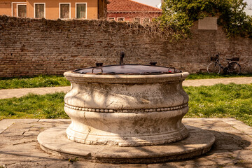 Burano old stone baroque well with a metal lid in the park, Venice, Venezia, Italy