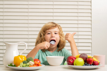 Kid preteen boy lick spoon in the kitchen at the table eating vegetable and fruits during the dinner lunch. Healthy food, vegetable dish for children.