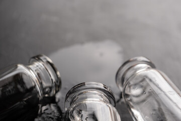 juego de tres frascos de vidrio con agua regada sobre madera negra con textura, monocromático