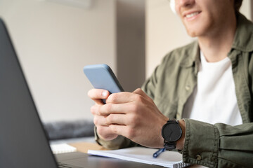 Closeup of male hand holds mobile phone while working on laptop selective focus