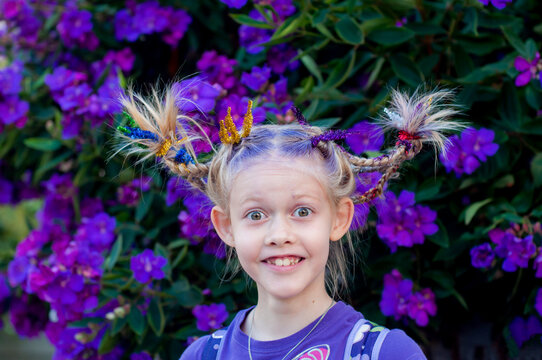 Funny Little Cute Caucasian Girl With Braids For Crazy Hair Day At School On Purple Flowers Tibouchina Nature Outside Background