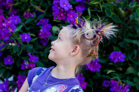 Funny little cute caucasian girl with braids for crazy hair day at school on purple flowers tibouchina nature outside background