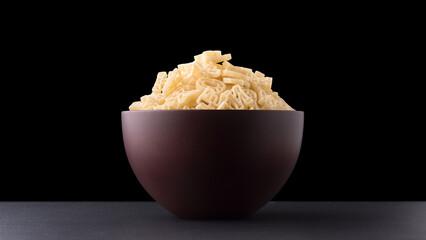 pasta letters or alphabet in a brown cup on black surface, black background, diet and food concept, side view 