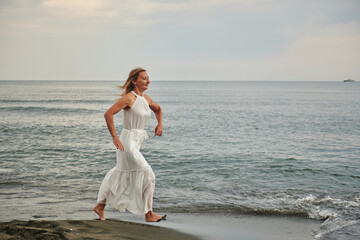 Fototapeta na wymiar a girl in a white dress runs along the shore