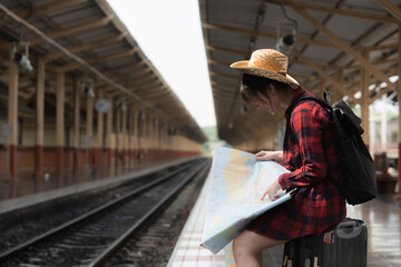 Pretty Young traveler woman looking on maps planning trip at train station. Summer and travel lifestyle concept.