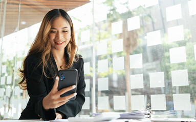 Asian businesswoman in formal suit in office happy and cheerful during using smartphone and working