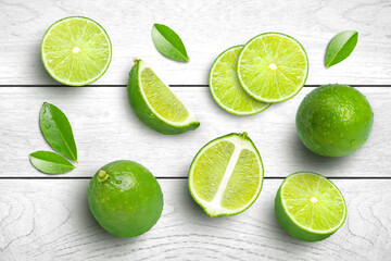 Fototapeta na wymiar Whole and half sliced green lime with leaves isolated on grey wooden table background. Top view. Flat lay.