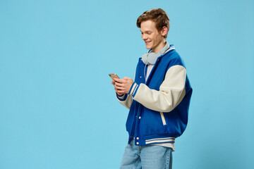 handsome young man in bomber jacket listening to music through headphones with phone in his hands