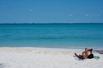 Fototapeta na wymiar A young woman relaxes lying on the deserted beach of a tropical island in Mexico