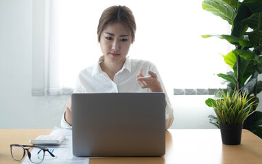 Asian businesswoman analyzes charts using laptop calculator at the office.