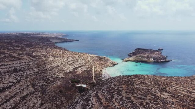 Aerial drone. Spiaggia and Isola dei Conigli, Lampedusa. Tranquil, cove-style beach with white sand and turquoise surf bordered by rocky cliffs.
