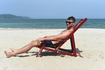 Young man drinking beer and sitting on deck chair at beach in Nha Trang