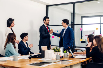 Fototapeta premium Image two asian business partners in elegant suit successful handshake together in front of group of casual business clapping hands in modern office.Partnership approval and thanks gesture concept