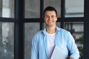Portrait of successful young businessman or entrepreneur standing in modern office. Happy...