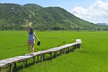 Fototapeta na wymiar A young woman walking across wooden pier in a rice field