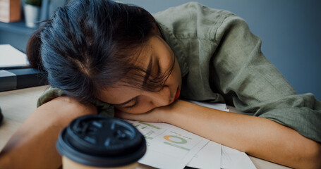 Freelance Asia exhausted lady hard work sleeping with many a paper coffee cup on wooden table at...