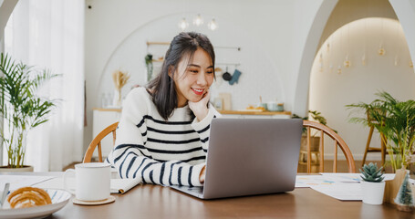 Young asia lady freelance focus on presentation work in laptop for account and finance project for remote meeting with company in kitchen at house. Girl student learn online at home.