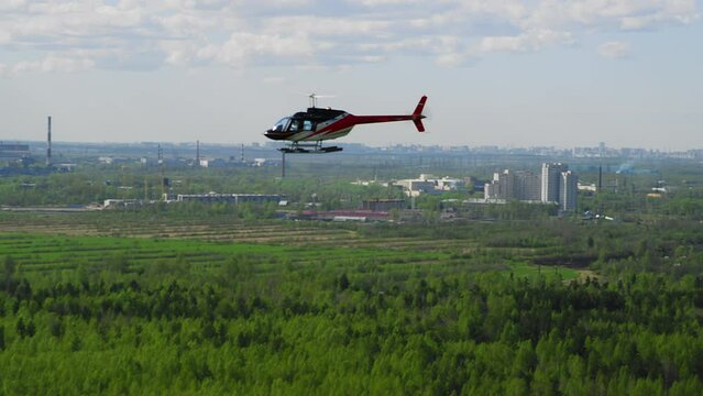 Helicopter blue white red colors flies against a background of blue sky and green fields and buildings on a sunny day. Bell helicopter flies in flight. film grain texture. Pixel texture. Defocus.