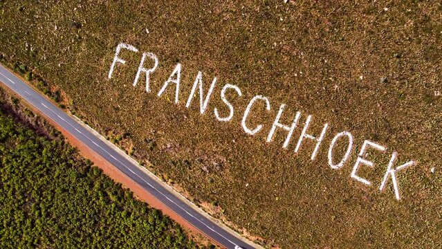 Car driving mountain pass and name of Franschhoek on mountainside; aerial