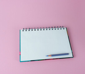 An open notebook with a blue pencil on a pink background. Concept - planning, daily routine.