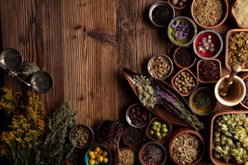  Natural medicine background. Assorted dry herbs in bowls and brass mortar on rustic wooden table.