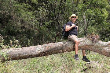 Dark-haired Latino adult man with hat, sunglasses, backpack, barmudas enjoys nature a moment of happiness, tranquility, well-being, relaxation, fullness
