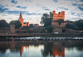 Final sunset ray highlights Rochester castle and cathedral. High visible evening sky and reflection on river surface.