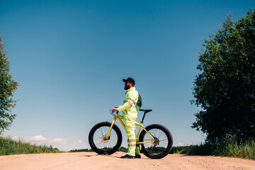 Naklejka premium Fat-tire bike in summer driving through the hills. Man is posing with a fat bike in the forest. He performs some tricks and runs dangerously. Bicycle with thick wheels in nature.