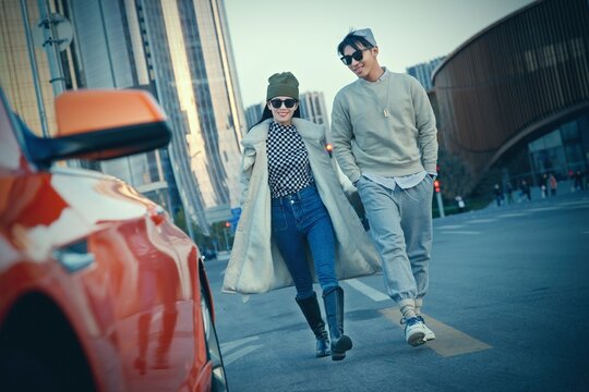 a Fashionable young couple with sunglasses and walking beside an orange luxury sports car