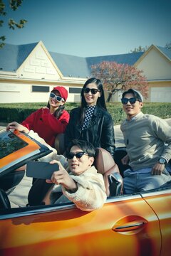 Young people use mobile phone take photo for four fashionable persons driving car to travel