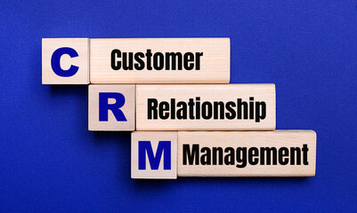 On a bright blue background, light wooden blocks and cubes with the text CRM Customer Relationship Management