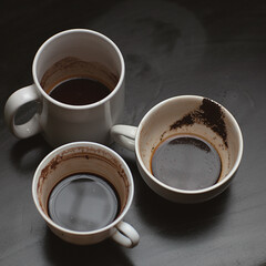 Dirty multi-colored cups, mugs, glasses after different types of coffee on a black wooden table left after morning coffee drinking , coffeeshop style