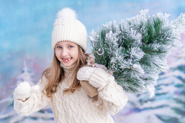 happy blue-eyed child girl in a hat and a knitted sweater, with a snow-covered Christmas tree on...
