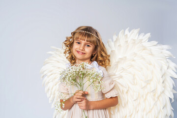 charming little girl with curly hair, dressed in an angel costume with big wings and flower crown....